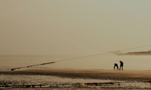 People walking on beach against clear sky