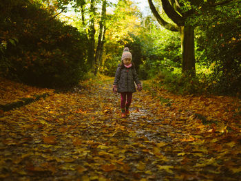 Full length of young  girl standing by leaves in forest