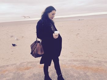 Beautiful young woman with coffee cup standing at beach