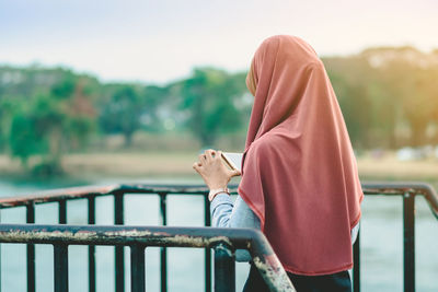 Side view of woman looking at railing against sky