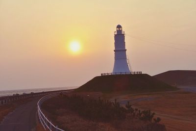 Lighthouse on landscape against sky at sunset