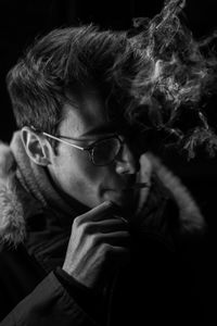 Close-up of young man smoking cigarette in dark