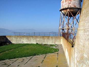 Water tower against sea against clear blue sky