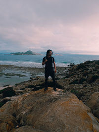 Full length of man standing on rock at sea shore against sky