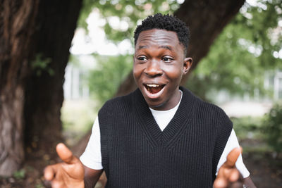 Shocked surprised young african man in park, smiling. fall or spring season