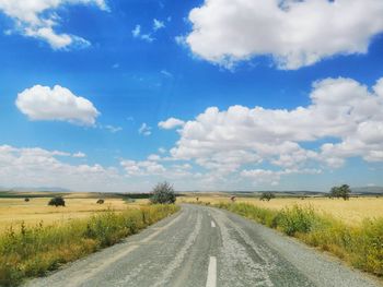 Empty road amidst field against sky