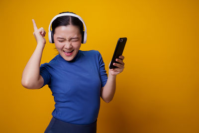 Young man using mobile phone against yellow background