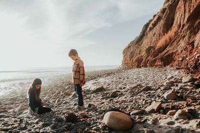 Rear view of boys on rock at beach against sky