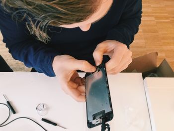 Directly above shot of man repairing smart phone while sitting at table