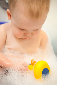 Close-up of shirtless baby boy in bathtub at bathroom