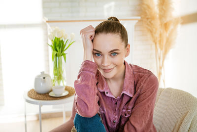 Happy calm young woman relaxing on comfortable armchair in living room, smiling