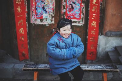 Portrait of smiling girl sitting on bench against wall