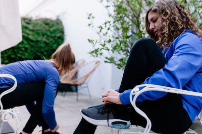 Side view of woman tying shoelace while sitting on chair