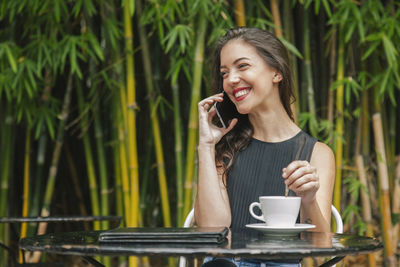 Smiling man holding coffee cup on smart phone outdoors