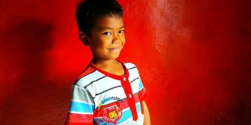 Portrait of boy standing against red wall