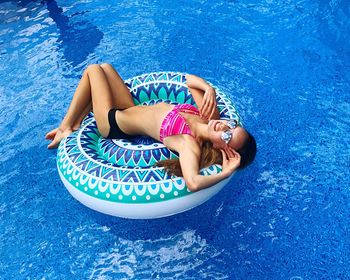 High angle view of woman wearing sunglasses while relaxing on inflatable ring at swimming pool