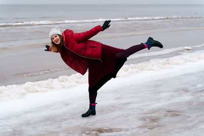 Cheerful woman on the beach in the arabesque pose in winter