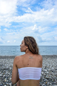 Rear view of woman sitting on beach against sky