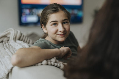 Portrait of smiling girl sitting on sofa by mother in living room