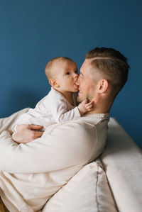 A six-month-old baby son in the arms of his happy father, trying to bite his nose