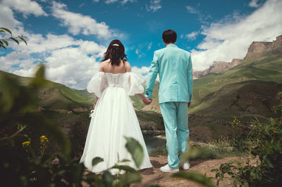 Beautiful newlyweds stand sideways to each other, holding hands against the backdrop of sunset