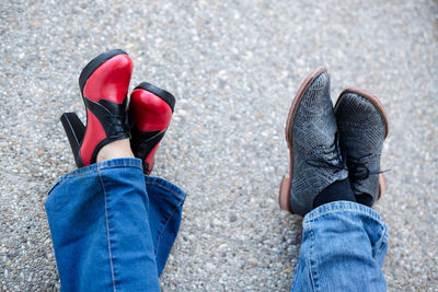 Low section of friends wearing shoes while sitting on road