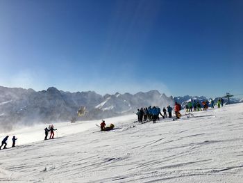 People on snow covered mountain against blue sky