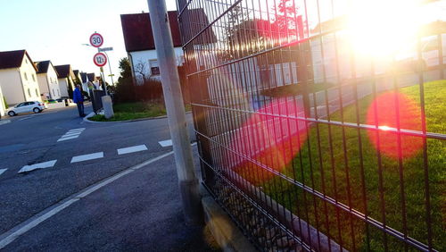 Road by fence in city against sky