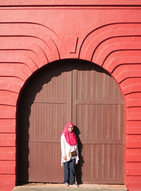 Full length of woman standing against red door