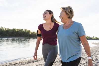 Fit grandmother and granddaughter walking at the river with arms around, having fun