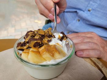 Midsection of man holding eating frozen yogurt bowl with banane, caramel and chocolate