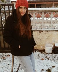 Portrait of smiling young woman standing against wall during winter
