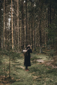 Woman standing by tree trunk in forest