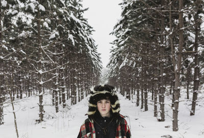 Portrait of confident teenage boy wearing warm clothing while standing in forest during winter