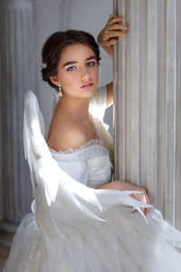 Portrait of a beautiful young woman in a white dress and angel wings, standing with a pleading look 