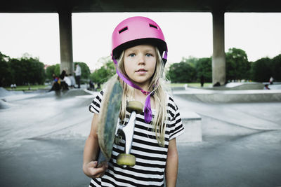 Portrait of girl holding skateboard while standing at park