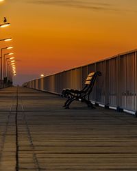 Empty bench on bridge against sky during sunset