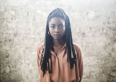 Portrait of confident female programmer with dreadlocks standing against wall in office