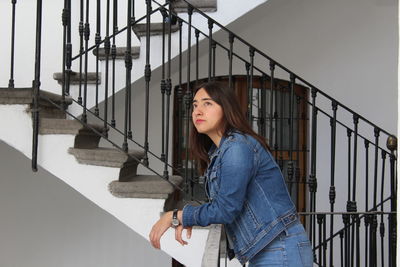 Portrait of young woman standing on steps against sky