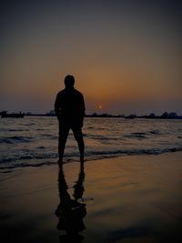 Rear view of silhouette man standing on beach during sunset