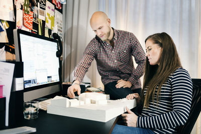 Business people discussing over model at computer desk