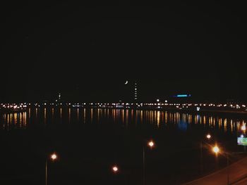 Illuminated city by sea against sky at night