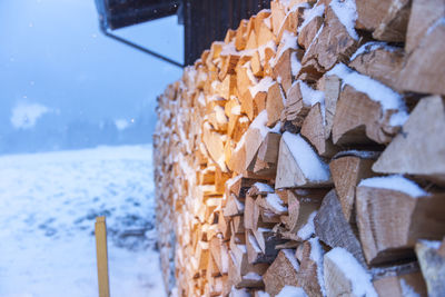 Full-sized side view of freshly beaten, stacked on a barn and snow-covered firewood in snowfall.