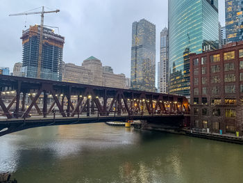 Bridge over river by buildings against sky in city