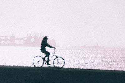 Silhouette man riding bicycle on snowy field against sky