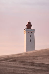 Lighthouse on beach by sea against sky