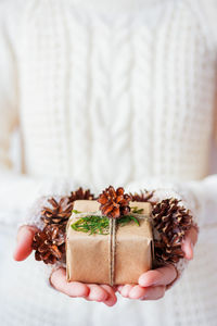 Woman in knitted sweater holding a present. gift is packed in craft paper with pine cones.  