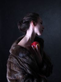 Side view of woman holding apple against black background