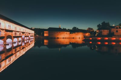 River by illuminated buildings against clear sky at night