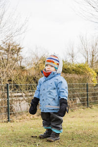 Full length of girl in warm clothing standing on field against sky